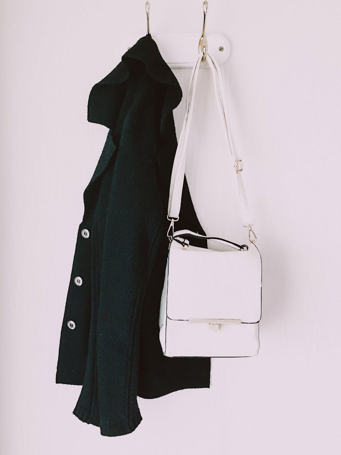 Stylish black jacket and white handbag on a wall hook. Fashion contrast display.